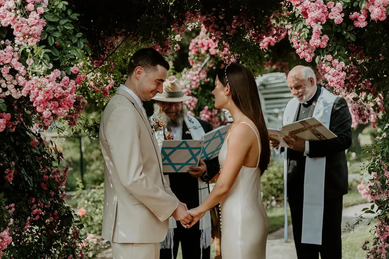 bride and groom holding hands while rabbi richard winer officiates ceremony